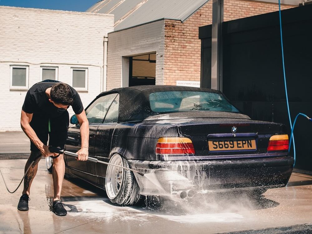シャワーホースを使って車を洗う男性